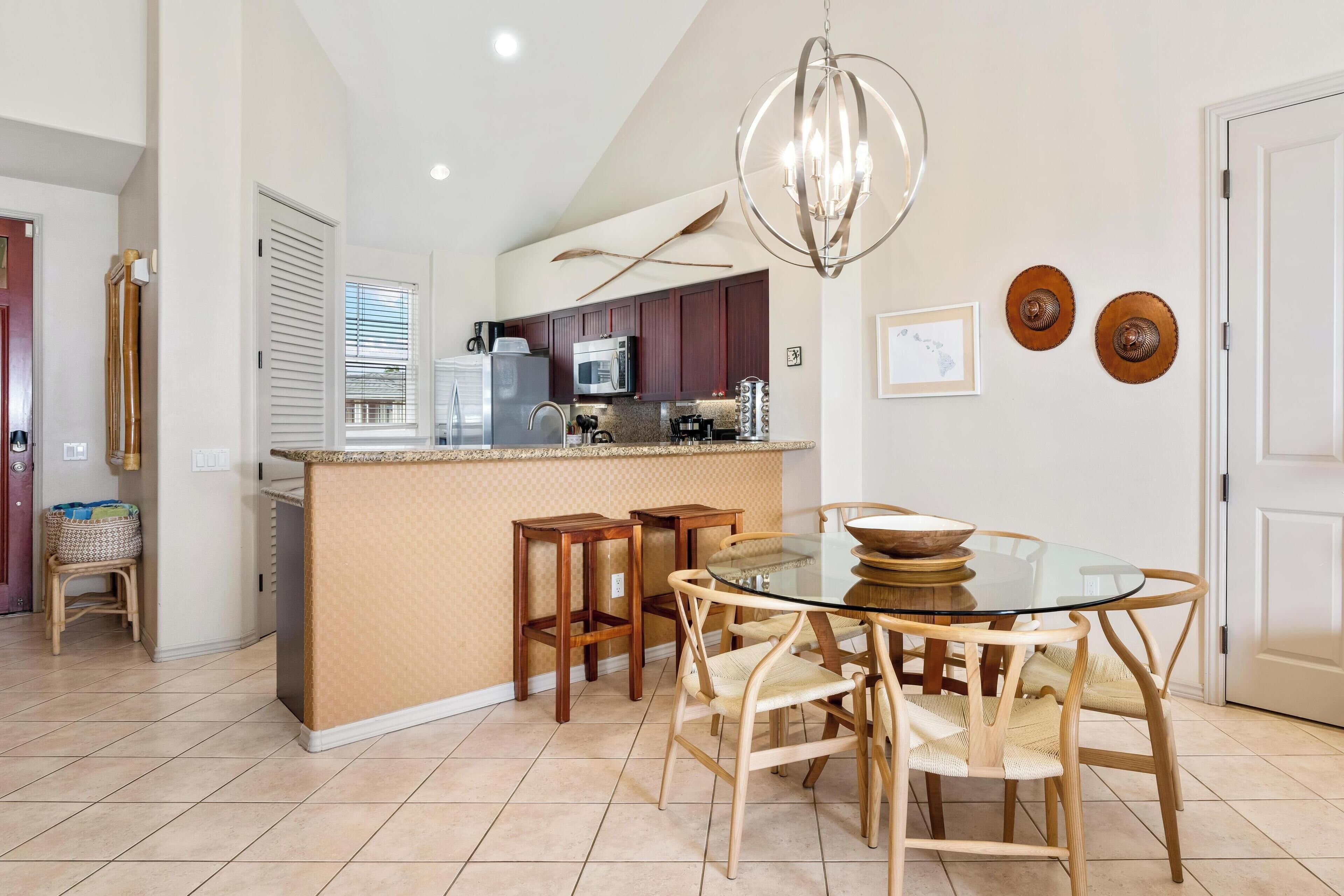 A modern kitchen with a glass island, wooden chairs, and a chandelier.