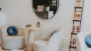 Uma sala de estar moderna com um espelho redondo, uma pequena mesa redonda com peças de xadrez e uma escada com revistas.