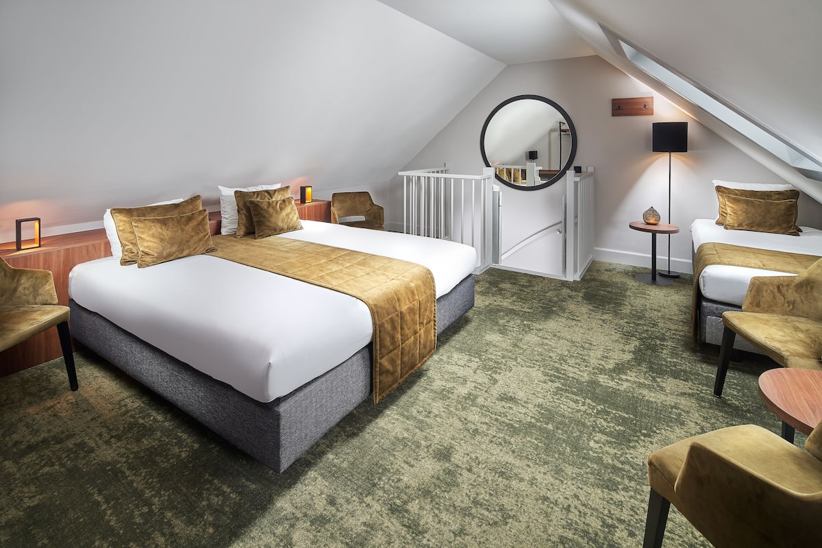 Una habitación de hotel moderna con una cama grande, un escritorio pequeño, una silla, un espejo redondo y un radiador.