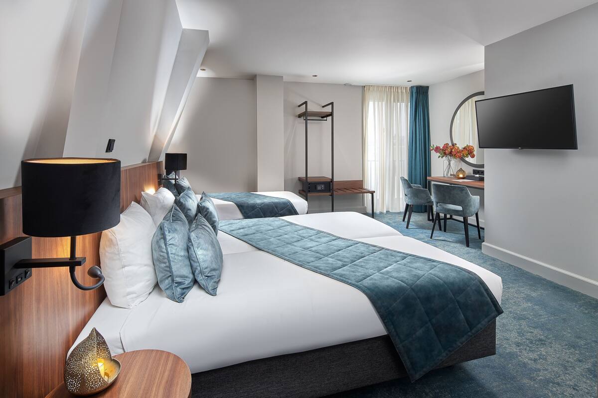 Habitación de hotel con cama, lámpara de noche, escritorio, silla, televisión y vistas al cielo.