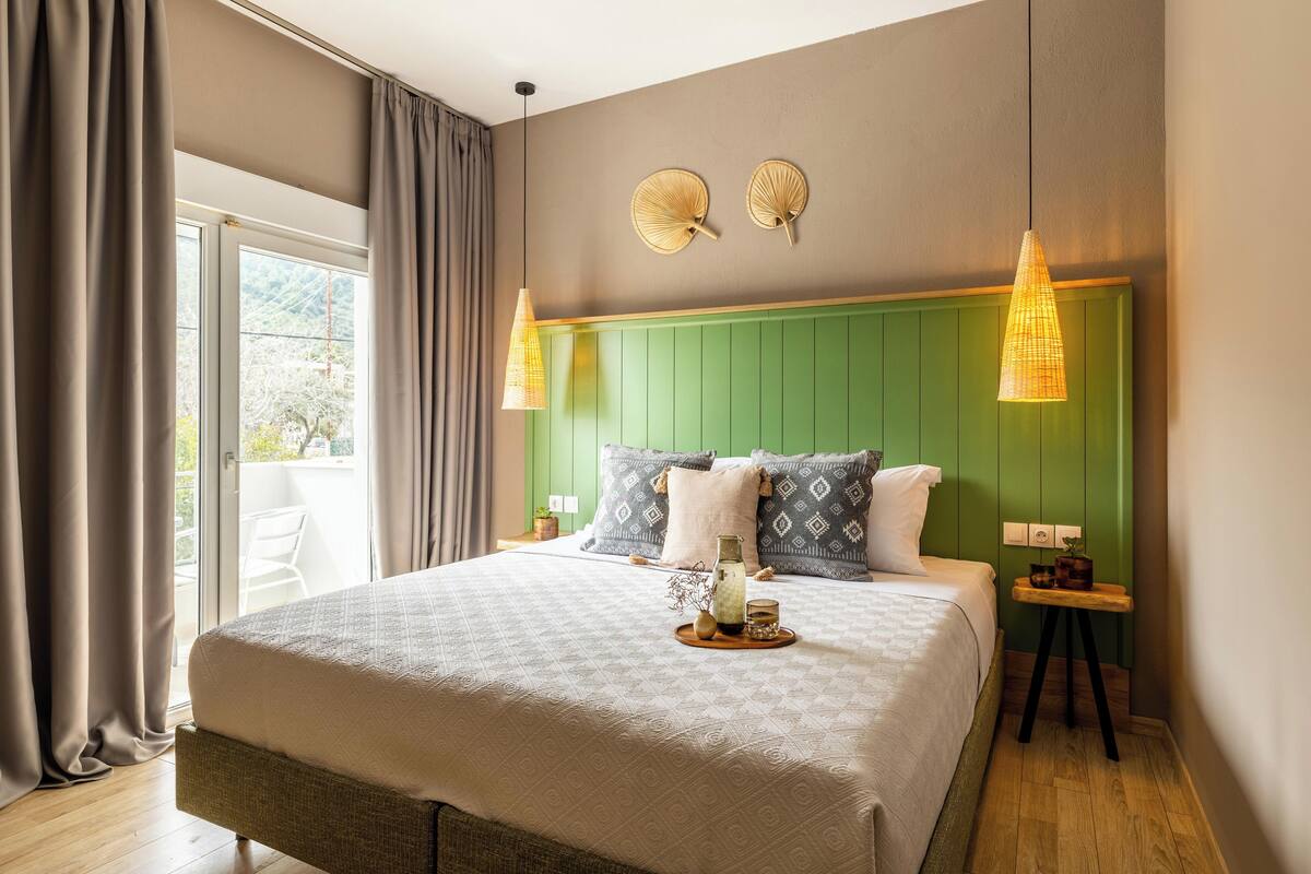 A bedroom with a large bed, green headboard, two wall-mounted lamps, and a small bedside table with a plant.