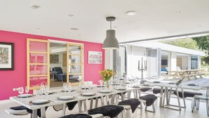 A modern dining area with a white table set for six, a large pendant light, and a pink wall. - Finest House In Cheltenham ! (Cheltenham)