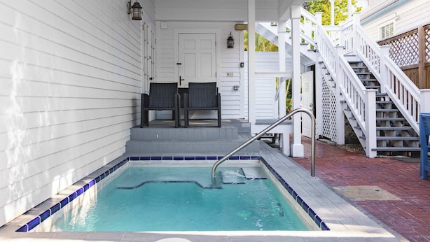 A small outdoor swimming pool with a metal ladder, surrounded by white walls and a wooden deck.