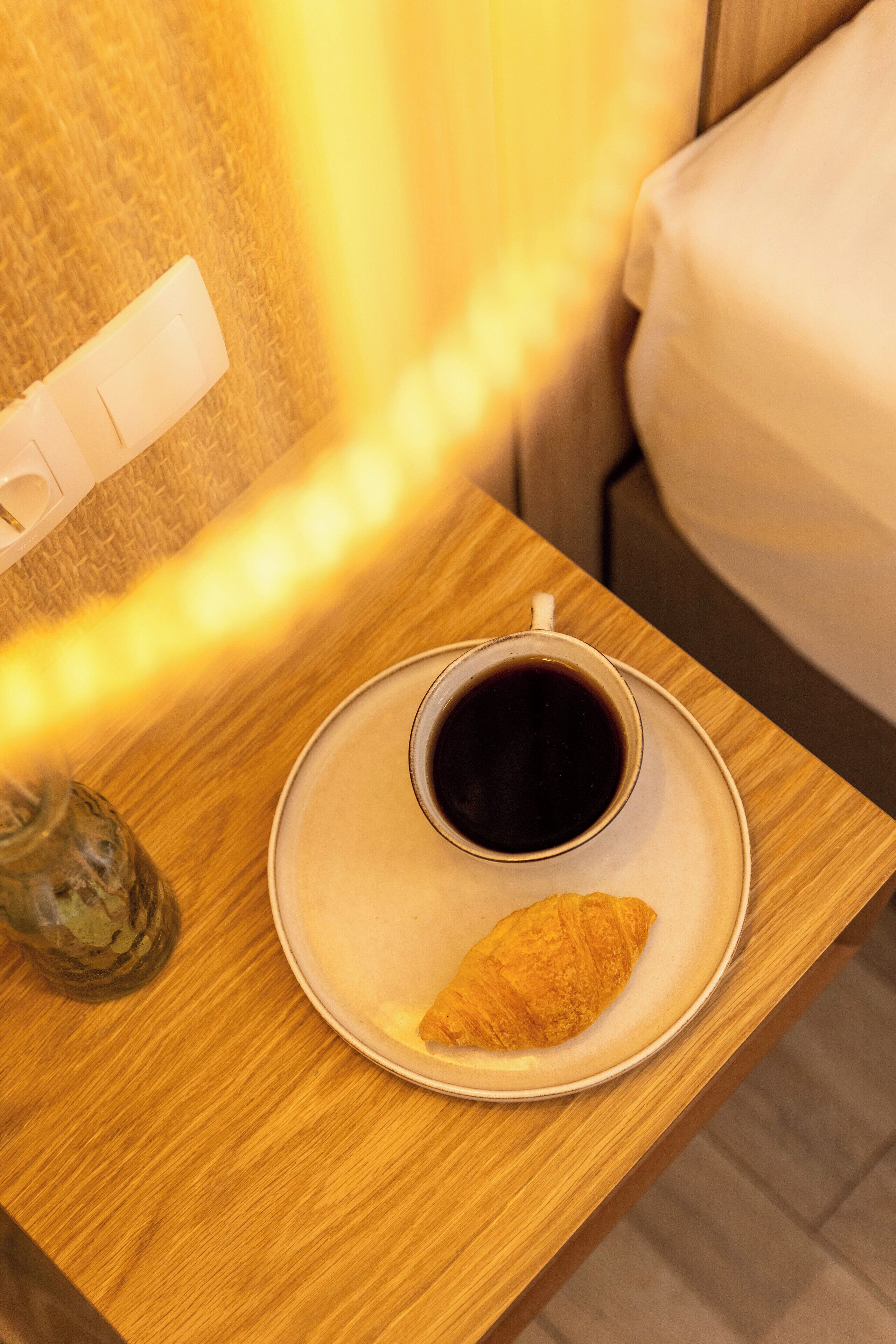 A wooden bedside table with a plate of croissant and a cup of coffee.