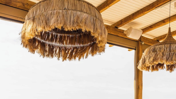 A dining area with a view of the sea, wooden furniture, and hanging thatched lamps. - Skiathos Thalassa Philian Collection (Skiathos)