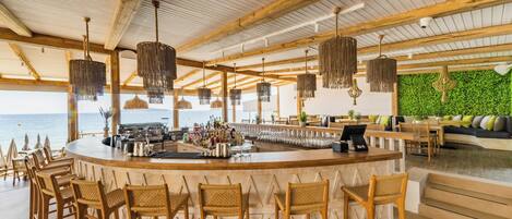 A bar area with wicker chairs, a bar counter, and a view of the ocean.