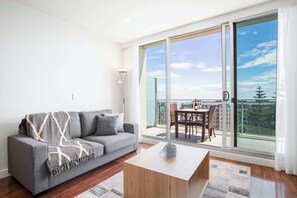 A modern living room with a grey sofa, a wooden coffee table, and a view of a balcony with outdoor furniture.