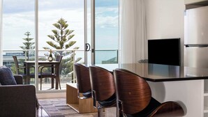 Habitació d'hotel moderna amb balcó, zona de menjador amb cadires, televisió i frigorífic.