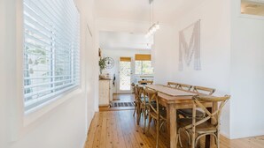 A dining area with a wooden table and chairs, a window with blinds, and a door leading outside. - Argyle Beach House by Book Jervis Bay (Vincentia)