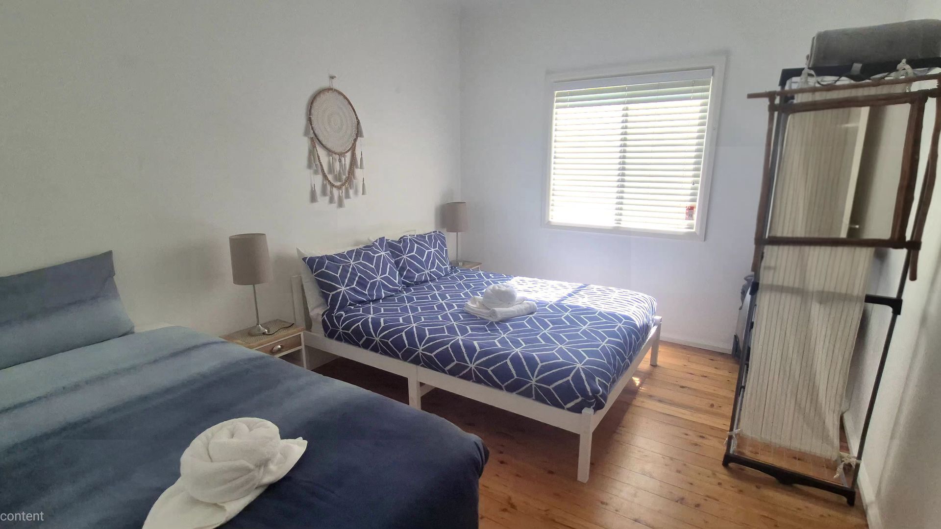 A bedroom with a bed, a wardrobe, a window with blinds, and a dreamcatcher on the wall.