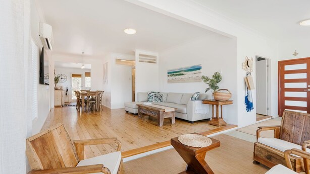 A spacious living area with a wooden floor, a sofa, a coffee table, and a dining table with chairs. - Argyle Beach House by Book Jervis Bay (Vincentia)