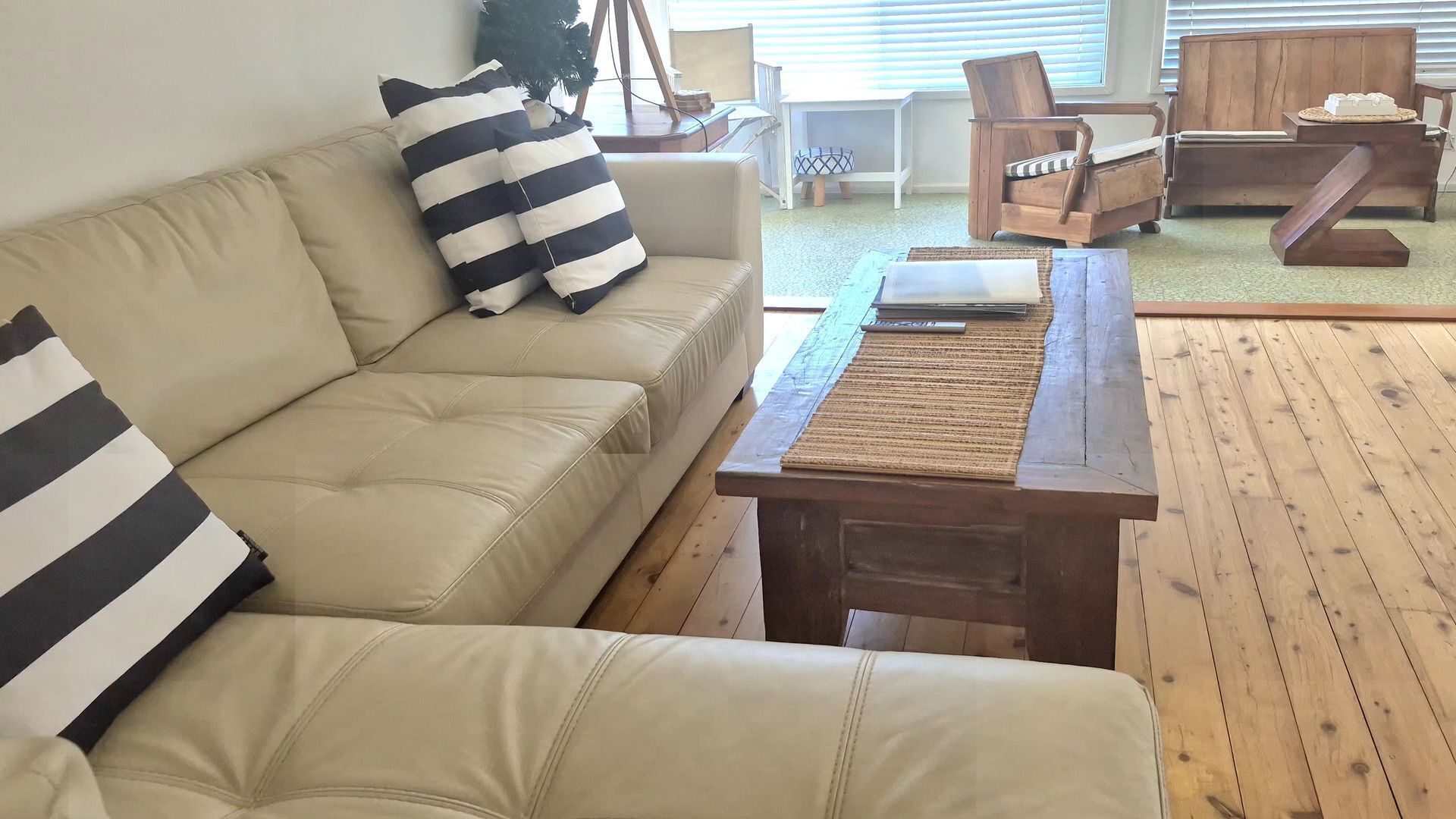 A living room with a beige sofa, striped pillows, a wooden coffee table, and a wooden floor.