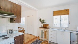 A modern kitchen with white cabinetry, a wooden dining table, and a built-in stove. - Argyle Beach House by Book Jervis Bay (Vincentia)