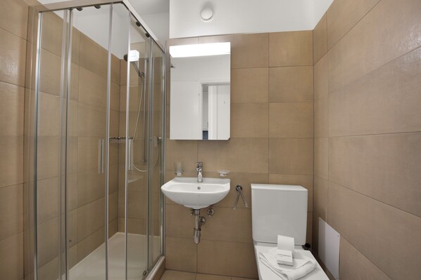 A modern bathroom with a glass shower enclosure, a white sink, and a toilet. - Locarno City Apartments (Locarno)