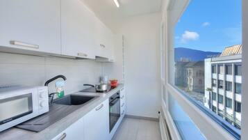 A modern kitchen with white cabinets, a microwave, a sink, and a window with a city view.