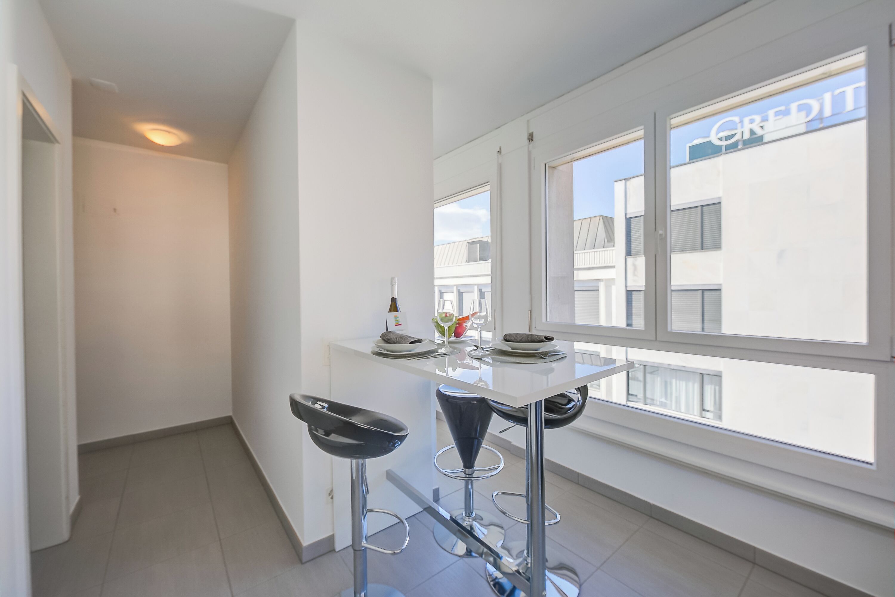 A modern kitchen with a white countertop, two bar stools, and a window with a view of buildings.