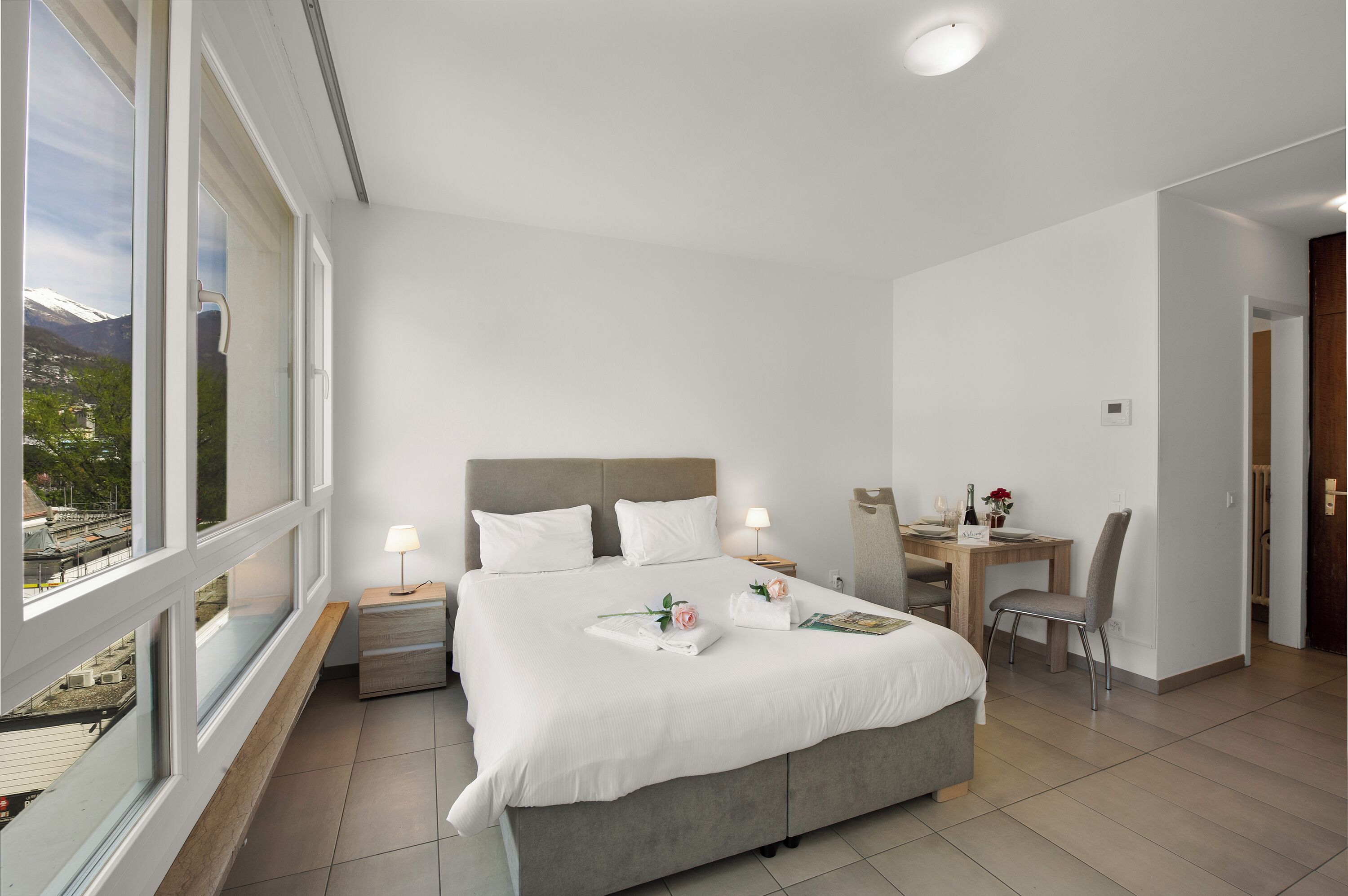 A hotel room with a large bed, a desk, and a chair. There is a window with a view of mountains.