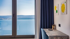 Una habitación con un ventanal grande, una silla azul, una mesa con un jarrón y dos cuadros abstractos en la pared.