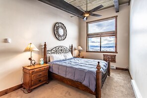 A bedroom with a wooden bed, two bedside tables with lamps, a large window with a view, and a ceiling fan.