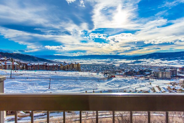 A panoramic view of a snowy landscape with buildings, a ski slope, and a clear sky.