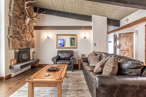 A living room with a stone wall, leather furniture, a fireplace, and a mounted deer skull.