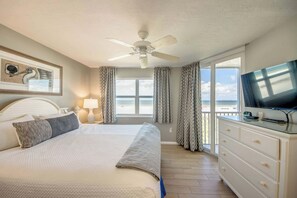 A hotel room with a bed, a television, a desk, and a view of the beach.