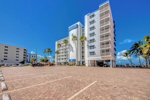 A modern hotel with a parking lot, multiple floors, and a clear blue sky.