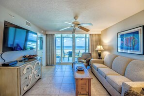 A hotel room with a balcony, a ceiling fan, a television, a sofa, and a painting.