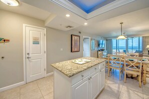 A modern kitchen with a granite countertop, white cabinetry, and a view of the ocean through large windows.