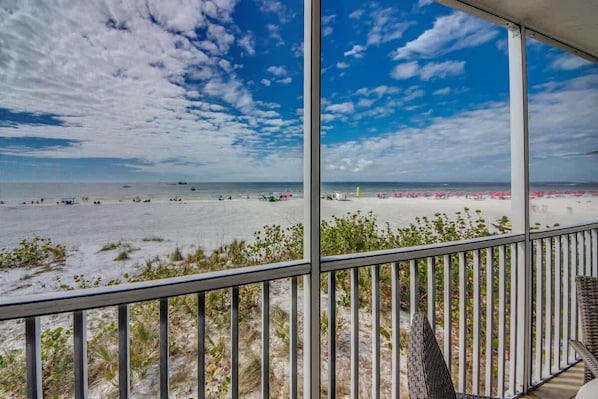 Une vue sur la plage depuis un balcon doté d’une balustrade, avec une plage de sable et l’océan en toile de fond.