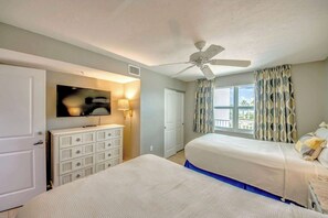 Une chambre d’hôtel avec deux lits, un ventilateur de plafond, une télévision, une commode et une fenêtre avec des rideaux.