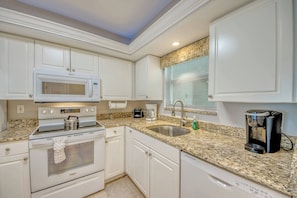A kitchen with white cabinetry, a microwave, a stove, a coffee maker, and a coffee machine.