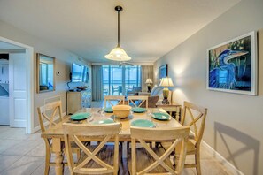 Un coin repas avec une table dressée pour quatre personnes, un ventilateur de plafond et une vue sur l’océan grâce à de grandes fenêtres.