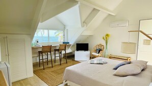 Een slaapkamer met een groot bed, een bureau met twee stoelen, een televisie en uitzicht op zee.