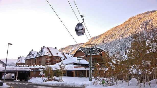 A ski lift with a cable car moving over a snowy landscape, a building with a sloped roof, and a road with snowbanks. - Val de Ruda Luxe 66 by FeelFree Rentals (Naut Aran)