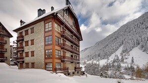 A multi-story wooden building with balconies, set against a snowy mountain backdrop. - Val de Ruda Luxe 66 by FeelFree Rentals (Naut Aran)