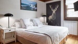 A bedroom with a bed, white bedding, two bedside tables with lamps, a window with a view, and two wall-mounted paintings. - Val de Ruda Luxe 66 by FeelFree Rentals (Naut Aran)