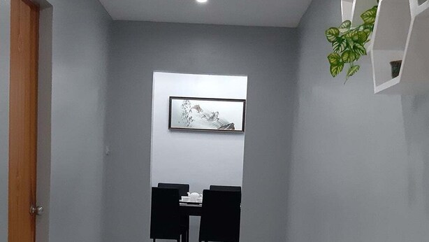 Un couloir moderne avec un sol brillant, une porte en bois sur la gauche et un coin repas avec des chaises noires et une table au centre.