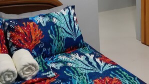 Une chambre à coucher avec un lit orné d’un motif coloré en forme de corail, un tableau représentant des arbres et une étagère hexagonale agrémentée de plantes.