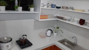 Une cuisine avec des meubles blancs, un évier, une bouilloire et différents ustensiles de cuisine rangés sur des étagères.