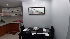 Une cuisine compacte avec un coin repas. Elle comprend un évier, un plan de travail avec divers ustensiles de cuisine et une table à manger avec des chaises. Une œuvre d’art encadrée est accrochée au-dessus de la table.