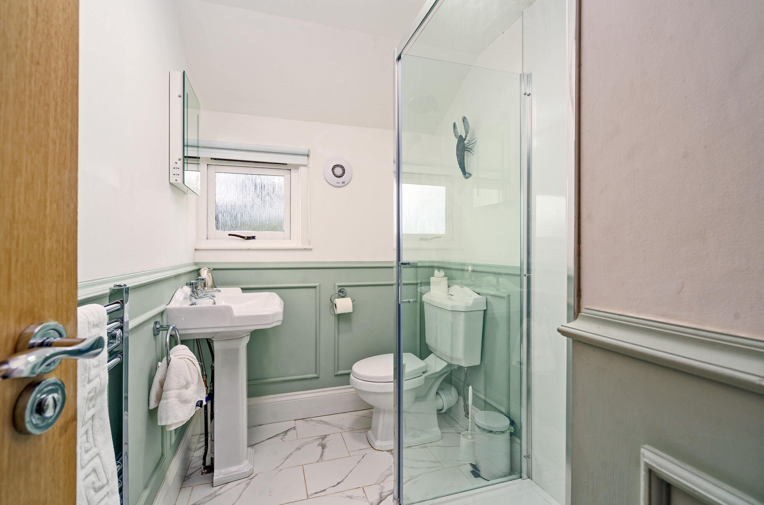 A bathroom with a glass shower enclosure, a pedestal sink, and a toilet.