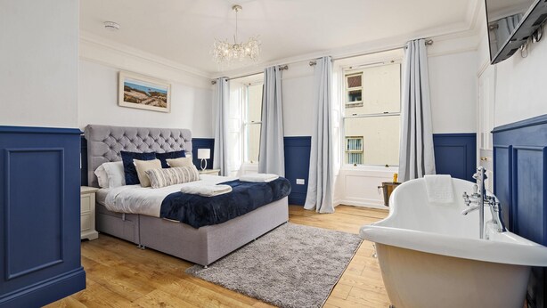 A bedroom with a large bed, a bathtub, and a view of the outside. - Clovelly House: Relaxed Family Coastal Home (Berwick-upon-Tweed)