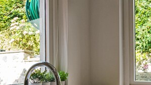A kitchen with a white sink, a window with a view of greenery, and a bowl of apples on the counter. - Clovelly House: Relaxed Family Coastal Home (Berwick-upon-Tweed)