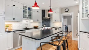 A modern kitchen with white cabinets, a black countertop island, red pendant lights, and a brick backsplash.