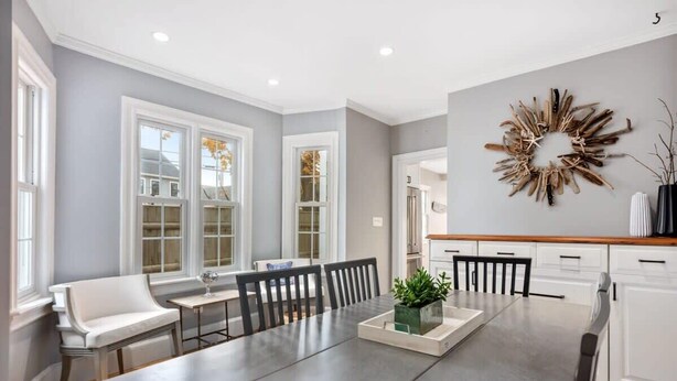 A modern dining area with a large table, white chairs, and a decorative wall piece.