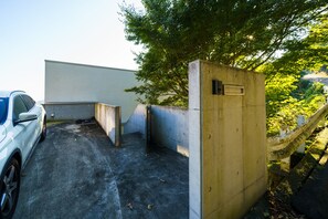 A parking area with a white car, concrete walls, and a tree providing shade. - Atami Hamada House (Atami)