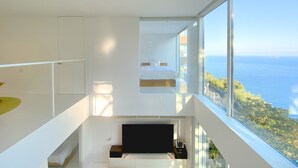 A modern bedroom with a large window overlooking the sea, a flat-screen TV, and a staircase leading to another level. - Atami Hamada House (Atami)