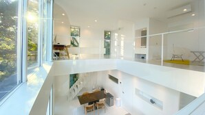 A modern interior with a dining area, a staircase, and a view of greenery outside. - Atami Hamada House (Atami)