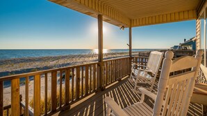 Une terrasse en bois avec des chaises Adirondack blanches donnant sur une plage.